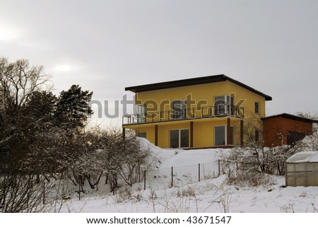 Uninhabited yellow rural cottage with red garage on a hill. The winter, the earth is covered by snow.