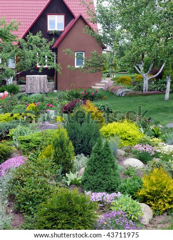 Fine flowers and ornamental shrubs near an accurate rural cottage.