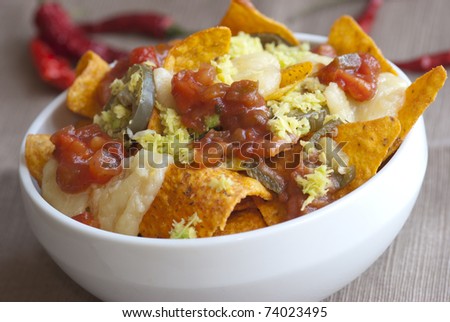 A bowl of vegetarian nachos with cheese, salsa sauce and jalapenos