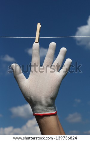 White gloved hand on clothesline against blue sky.