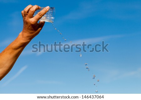Hand, glass and water against blue sky.