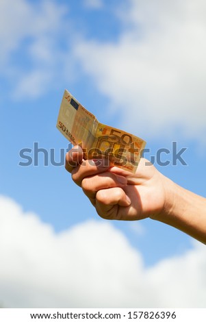 Money in hand against sky.