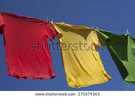 Wet shirts on clothesline against blue sky.