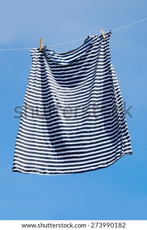 Wet striped shirt on clothesline against blue sky.