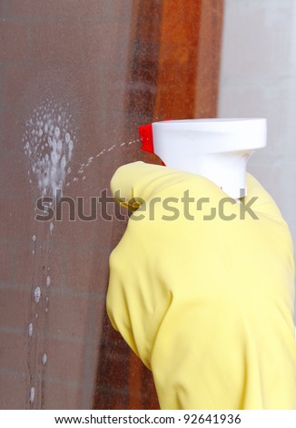 Hand spraying washing liquid on glass.