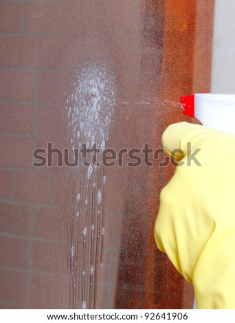 Hand spraying washing liquid on glass.