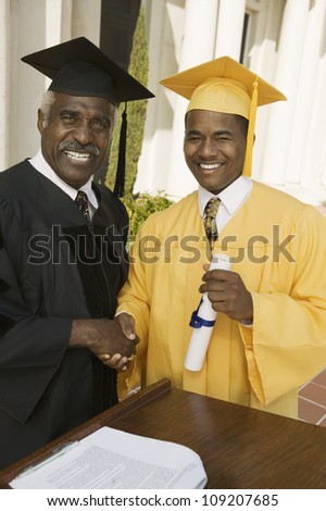 Happy young graduate shaking hand with dean at podium