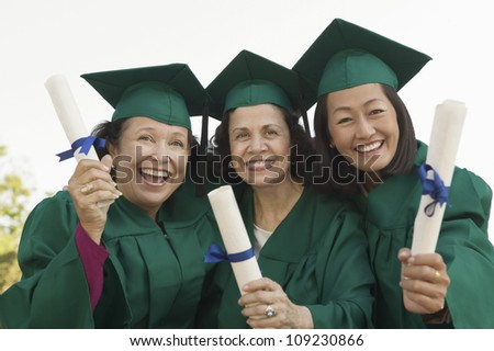 Group portrait of three multiethnic women in graduation gown holding degrees