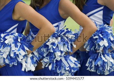Midsection of young female cheerleaders holding pom-poms