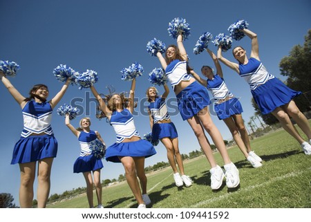 Group of excited young cheerleaders cheering on field