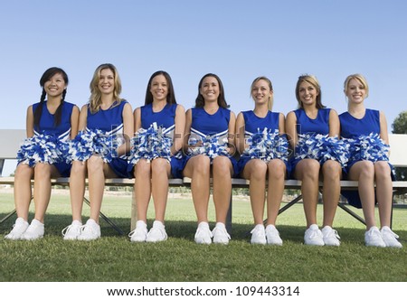 Group of young female cheerleaders sitting side by side on bench
