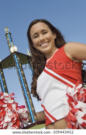 Portrait of a beautiful young female cheerleader holding trophy