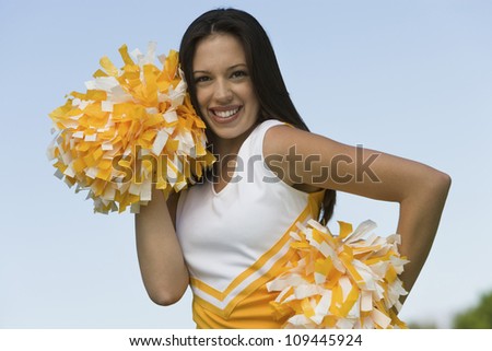 Portrait of a young beautiful cheerleader holding pom-poms