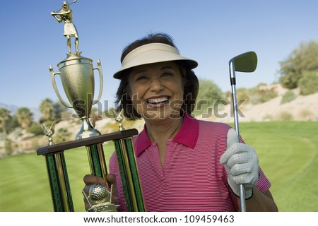 Portrait of a happy senior woman holding winning trophy at golf course