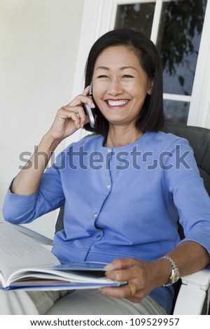 Happy mature woman sitting in chair with magazine using cell phone
