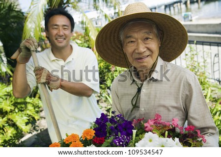 Portrait of a happy elderly man with son working in garden