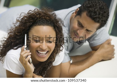 Cheerful African American woman using cell phone with man looking at her