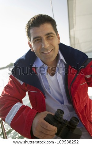 Portrait of a happy mature man holding binoculars on the yacht