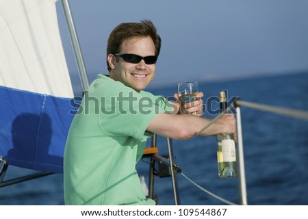 Happy man holding wine glass and bottle while sitting on the yacht