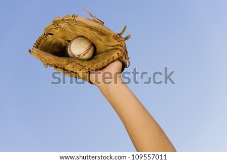 Hand of baseball player with glove and ball against clear sky