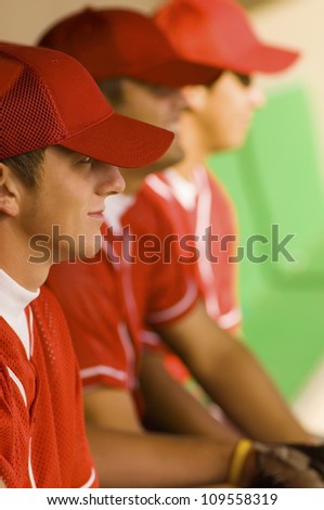 Side view of baseball players watching the game while sitting in dugout