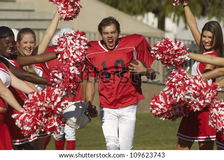 Portrait of excited american football player with cheerleaders cheering for him