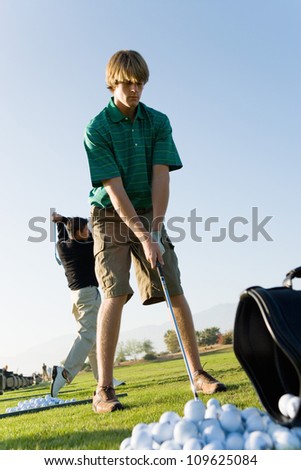 Full length of a young man playing golf with person in background