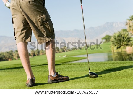 Low section of a young man with golf club on meadow