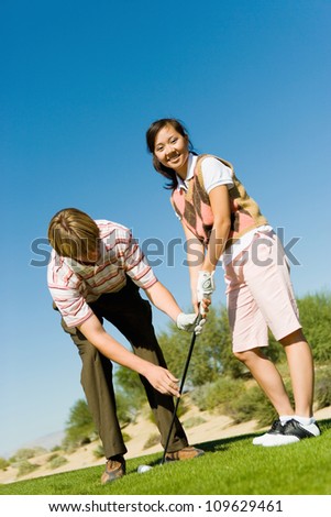 Portrait of a happy young woman learning golf from man on golf course
