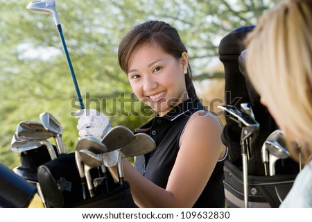 Portrait of a happy young woman picking up golf club from bag
