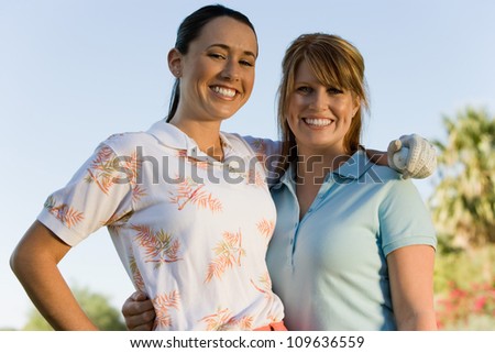 Portrait of happy female friends standing with arm around on golf course