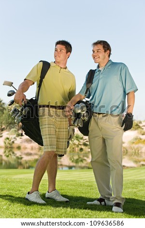 Full length of two male golfers carrying golf bags on golf course