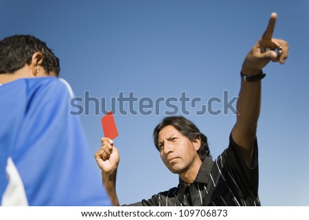 Low angle view of soccer referee pointing dismissal of player with red card