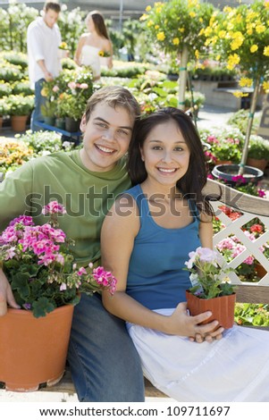 Portrait of a happy young couple with potted flower plants sitting on bench at botanical garden