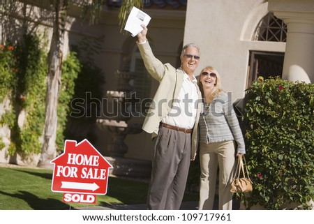 Excited couple standing in front of house with a For Sale Sold sign
