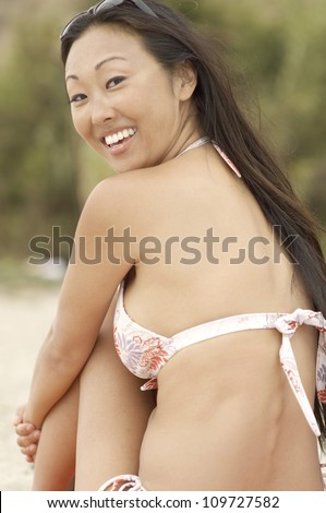 Portrait of an happy young Asian female in bikini sitting at beach
