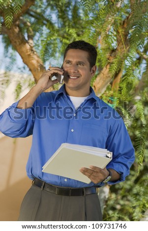 Happy mature businessman holding file folder while on call