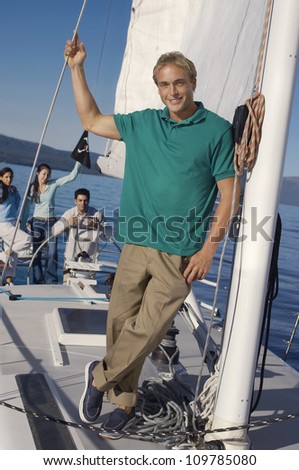 Full length portrait of Caucasian man standing in sailboat with friends in background