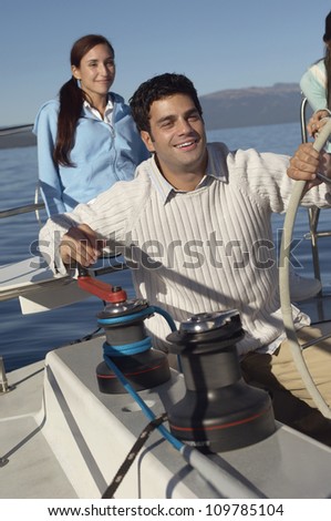 Man holding the steering of sailboat with friend in the background
