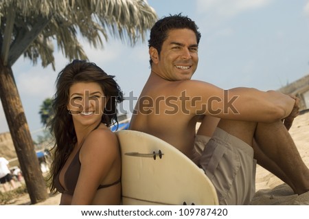 Portrait of happy man and woman sitting back to back on beach