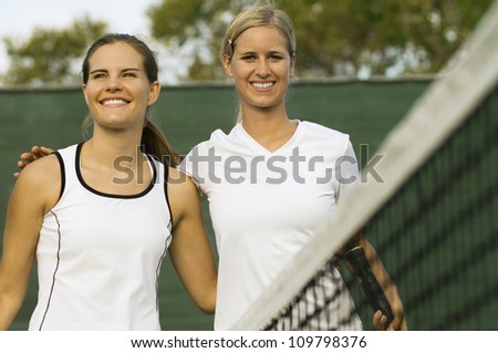 Portrait of happy tennis player standing arm around with her partner