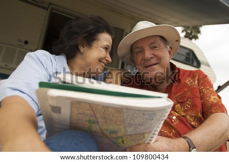 Happy senior couple holding map book with caravan in the background