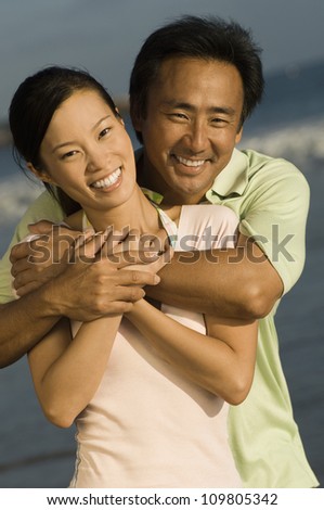 Happy asian man embracing woman from behind on the beach
