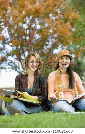 Two friends studying sitting together with books in park