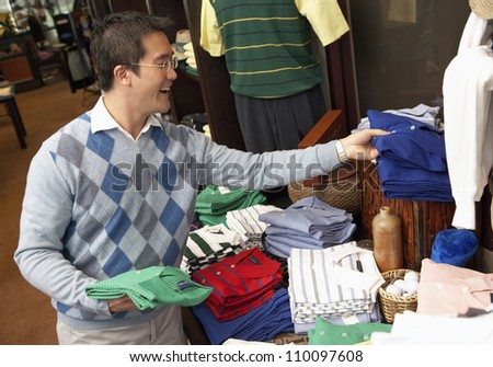 Happy Chinese man buying shirts in clothing store