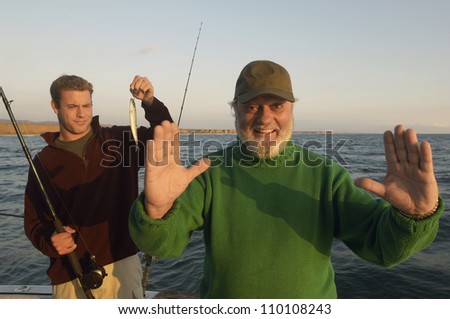 Happy senior man gesturing and person with small catch on yacht