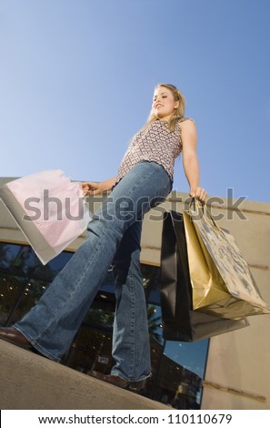 Low angle view of young woman carrying shopping bags in front of store