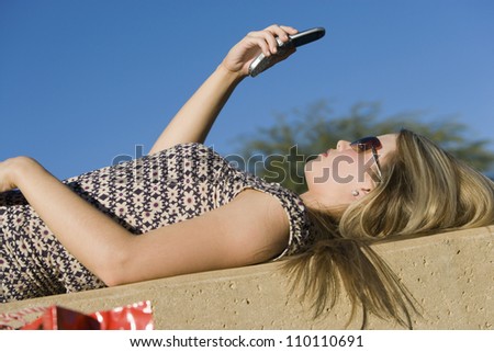 Side view of woman lying on back reading text message through cell phone