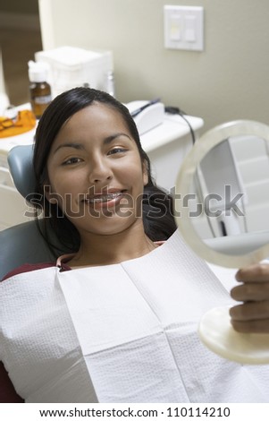 Portrait of happy female patient at dental clinic holding a mirror