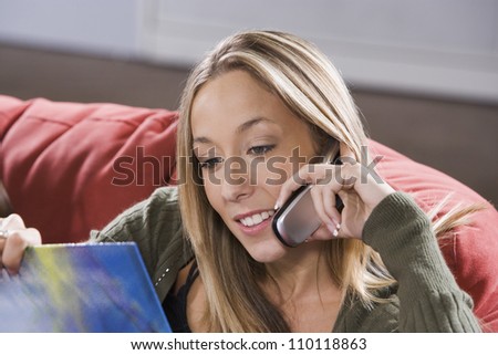 Young Caucasian female on couch reading book while talking on the phone